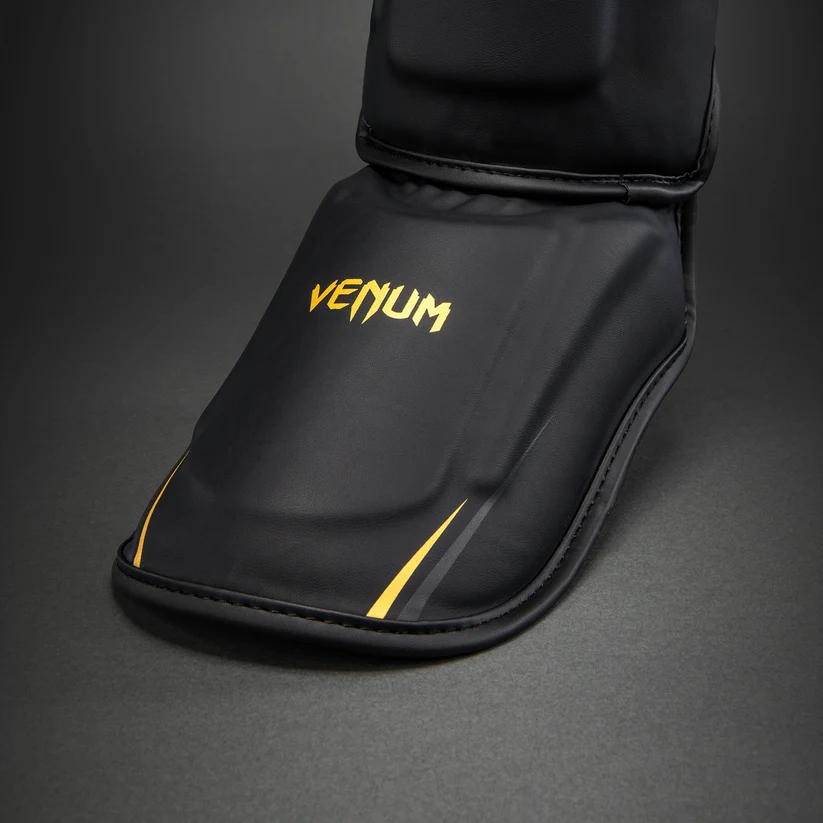 Paratibie Venum G-Core Nero/Oro VENUM-06400-126 per allenameti di Muy Thai, kickboxing ed MMA. Paratibie strutturato da allenamento con chiusura in velcro stabile e solido.